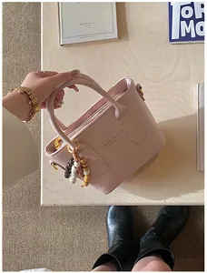 Detailaufnahme der rosa Leder-Beuteltasche mit Modedruck und Perlenanhänger auf Holz