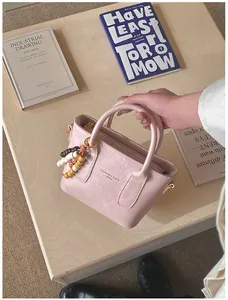 Nahaufnahme der hellrosa Lederhandtasche mit Goldbeschlägen und Perlen-Anhänger-Detail