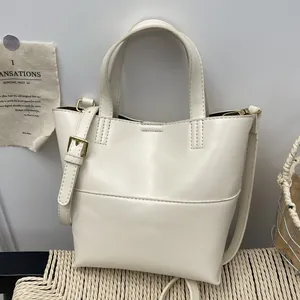 Minimalist white bucket bag with top handles and adjustable strap on textured background