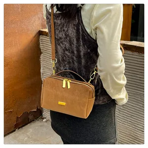 Macro detail of brown suede crossbody bag featuring elegant gold double zipper closures