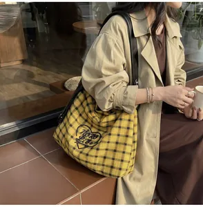 Side view of a large yellow plaid canvas tote bag with black straps and heart embroidery