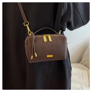 Detail of a dark brown suede Boston bag with gold hardware and knotted tassel accent