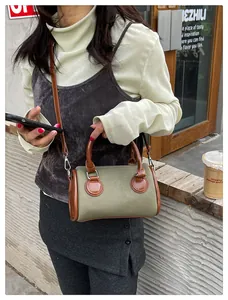 Vista de detalle del bolso cilíndrico de lona oliva y cuero marrón con un vestido gris