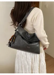 Detailed macro view of dark grey soft leather texture and hanging wooden bead tassel on tote bag