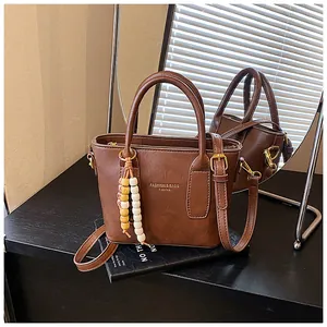 Nahaufnahme der braunen Retro-Beuteltasche mit Goldaufdruck und buntem Perlenanhänger