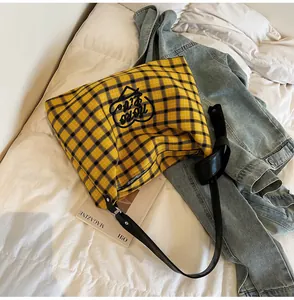 Detail of yellow plaid tote bag featuring heart embroidery and leather straps on white bedding