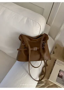 Bolso tote de cuero marrón retro con hebilla plateada sobre un sofá blanco