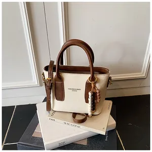 Detail der creme-braunen Handtasche mit Perlenanhänger auf einem Stapel Magazine