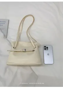 Detalle del bolso de hombro de cuero crema con comparación de tamaño con móvil