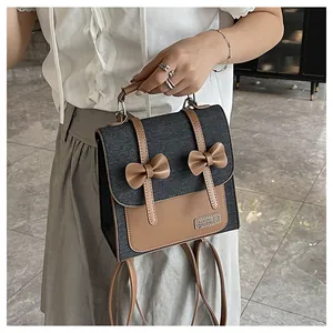 Detail of denim backpack with brown leather bows and metal logo on the front flap