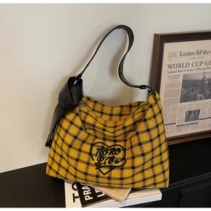 Detail of yellow checkered tote bag featuring heart embroidery and knotted shoulder strap