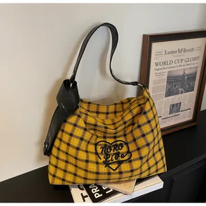 Detail of plaid tote bag featuring black heart embroidery and knot leather strap detail