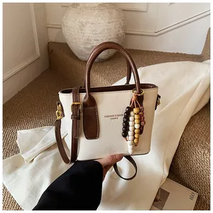 Detailansicht der beigen Tasche mit Holzperlenanhänger und braunen Lederriemen