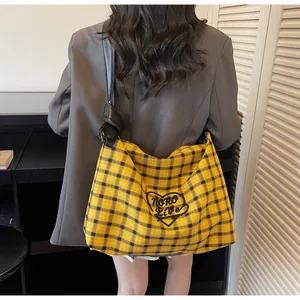 Close-up of yellow plaid tote bag featuring heart logo and black leather knotted strap