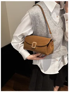 Detail of caramel suede crossbody bag with gold metal clasp on a stylish model outfit