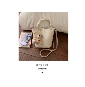 Detail van crème bucket bag met lychee textuur en beerhanger op houten vloer