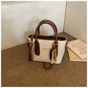 Detail einer Retro-Mini-Eimertasche aus cremefarbenem Kunstleder mit braunem Kontrast