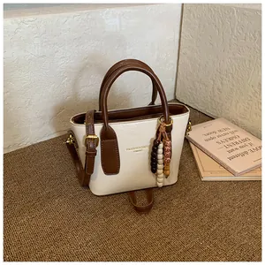 Detail der beigen Kunstledertasche mit braunen Riemen und Anhänger aus Holzperlen