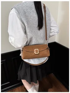 Close-up of brown suede crossbody bag with gold buckle on model in minimalist setting