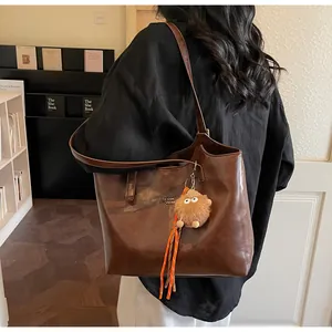 Close-up of deep brown tote bag with smooth faux leather texture and plush monster charm