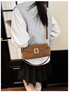 Detail of dark brown suede shoulder bag featuring a gold buckle on minimalist flap