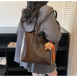 Detailed close-up of dark brown vintage tote bag with metal logo and plush monster charm