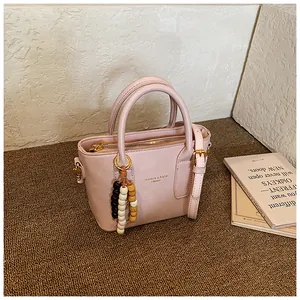 Rosa PU-Lederhandtasche im Detail mit Holzperlen-Anhänger und elegantem Front-Logo