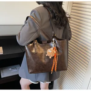 Détail du sac cabas marron foncé avec boucle métallique et breloque peluche monstre