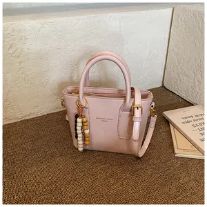 Detailansicht der rosa Trapez-Handtasche mit Perlenanhänger und Metallreißverschluss