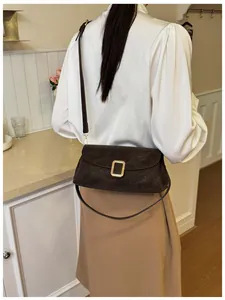 Detail of dark brown faux suede square bag with golden buckle on elegant model