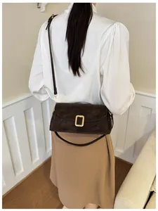 Detail of dark brown suede crossbody bag with gold buckle and adjustable strap