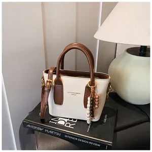 Detailansicht der cremeweißen Retro-Handtasche mit braunen Kontrastgriffen und Perlenanhänger