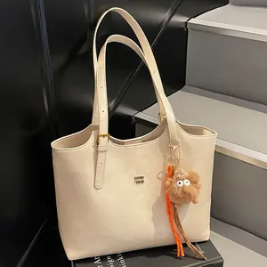 Large beige matte leather tote bag with a metal logo and brown plush pendant accessory