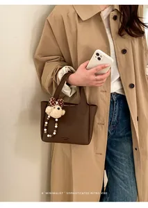Detail of dark brown leather bucket bag with cute bear charm held by model in trench coat