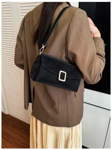 Detail of a black square shoulder bag with gold buckle on a model in a brown blazer