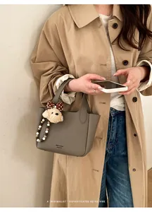 Close-up of grey litchi leather bucket bag featuring a plush dog charm and beaded strap