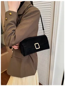 Detail of a black suede-textured rectangular shoulder bag with elegant gold metal buckle