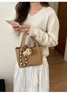 Detail of a brown leather bucket bag with a plush bear charm and beaded strap