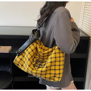 Close-up of a yellow checkered canvas tote bag with a black heart-shaped logo and leather strap
