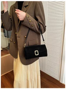 Detail of a black matte crossbody bag with a gold square buckle shown on a model