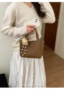 Close-up of brown bucket bag in lychee leather with plush bear and beaded strap