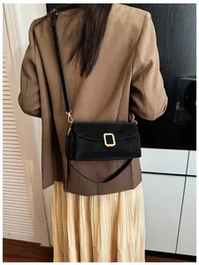 Detail of a black square leather crossbody bag with minimalist gold buckle on a model