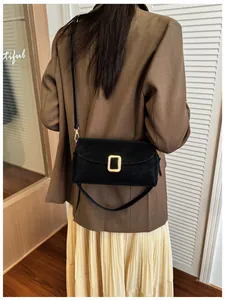 Detail of a vintage black suede crossbody bag with a gold buckle on a shoulder strap