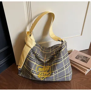Detail of yellow heart embroidery on plaid canvas tote with wide leather strap