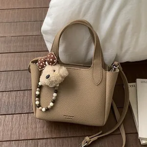Khaki leather bucket bag with beaded handle and cute plush bear charm for casual styling