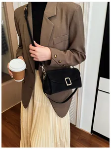 Detail of black matte leather crossbody bag with oversized gold buckle on brown blazer