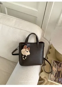 Detail einer dunkelbraunen Bucket Bag aus Leder mit einem süßen Plüschbären-Anhänger