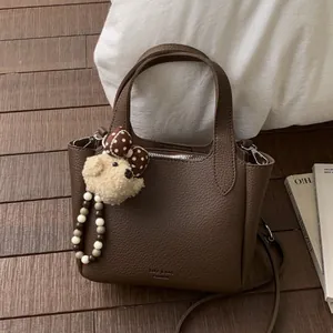 Deep brown pebble leather bucket bag with cute bear charm on a vintage wooden floor