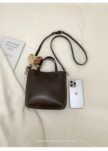 Detailansicht der dunkelbraunen Retro-Eimertasche mit Plüschbär auf weißem Stoff