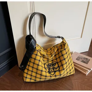 Detail view of yellow plaid tote bag featuring black heart embroidery and knotted leather strap